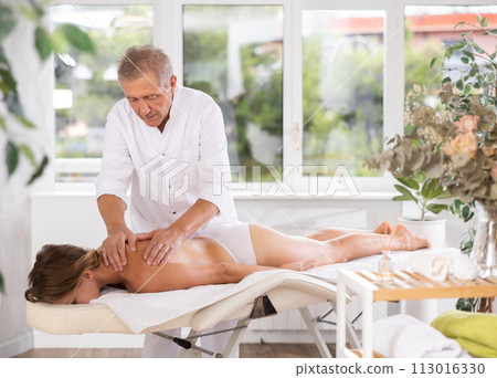 Skilled old masseur conducting back massage for woman client Skilled old masseur conducting back massage for woman client 113016330