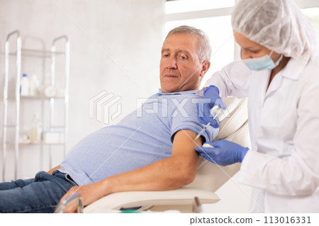 Elderly man getting intramuscular injection in upper arm in medical office Elderly man getting intramuscular injection in upper arm in medical office 113016331