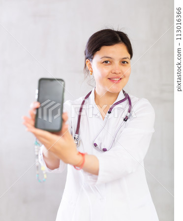 Smiling female doctor recommending mobile app on smartphone Smiling female doctor recommending mobile app on smartphone 113016366