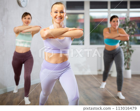 Class of positive young women in sportswear performing expressive movements during joint workout in dance hall 113016479