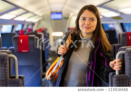 Smiling female backpacker standing in aisle between train seats 113016488