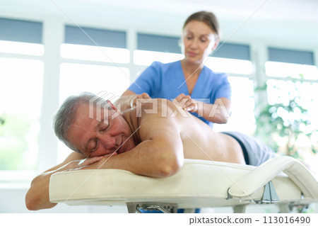 Relaxed old man having back massage therapy conducted by skilled masseuse Relaxed old man having back massage therapy conducted by skilled masseuse 113016490