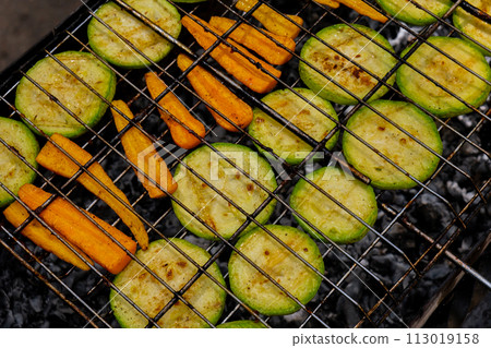 Chopped zucchini and carrots roasting on fire seasoned with aroma herbs and spices. Delicious fresh vegetables grilling on barbecue smoker grid. Diet vegan bbq. Outdoor recreation 113019158