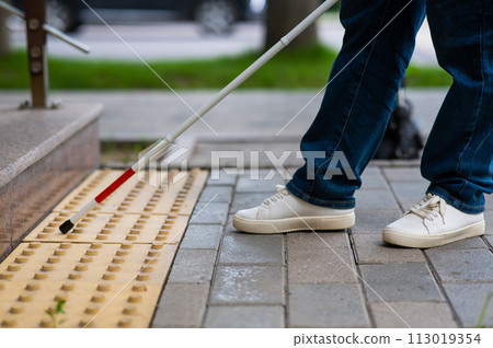 Close-up of female foot, walking stick and tactile tiles. Blind woman climbing stairs using a cane.  113019354