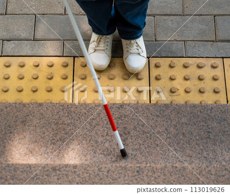 Blind woman walking outdoors using a tactile cane.  113019626