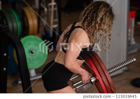 Middle-aged woman doing abdominal rows on a machine in the gym. Middle-aged woman doing abdominal rows on a machine in the gym. 113019645