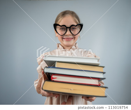 Little girl with glasses holding a stack of books on a white background.  113019754