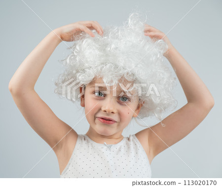 Portrait of a little Caucasian girl wearing a white curly wig on a white background.  113020170