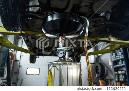 The process of changing the oil in a car engine. Draining old dark used oil from a car on a lift. The process of changing the oil in a car engine. Draining old dark used oil from a car on a lift. 113020251