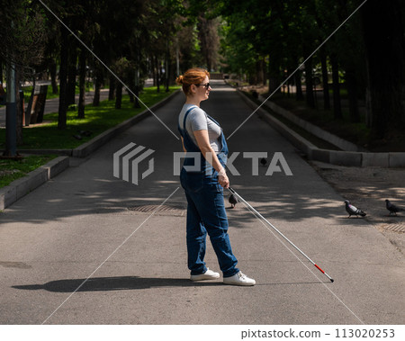 Blind pregnant woman crosses the street with the help of a tactile cane. 113020253