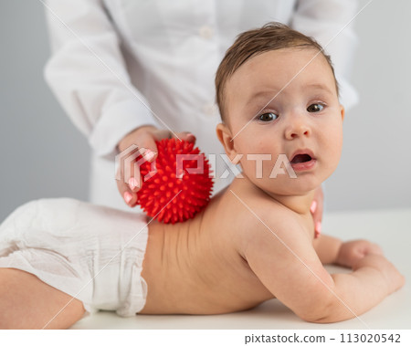 A doctor gives a child a back massage using a ball. 113020542