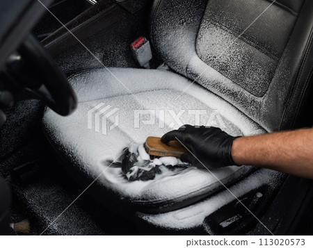 Man cleaning black leather car seat with brush and cleaning foam. Man cleaning black leather car seat with brush and cleaning foam. 113020573
