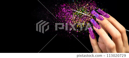 Hand with bright manicure and a brush on a black background strewn with sparkles. Nail design. Extended nails. Hand with bright manicure and a brush on a black background strewn with sparkles. Nail design. Extended nails. 113020729