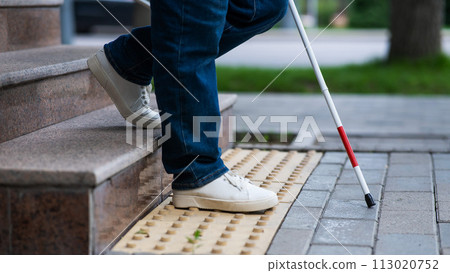 Close-up of female foot, walking stick and tactile tiles. Blind woman walking down stairs using a cane.  113020752