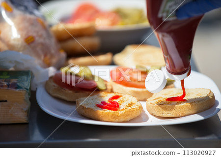 Cooking a hamburger. Ketchup is being poured onto the hamburger bun. 113020927