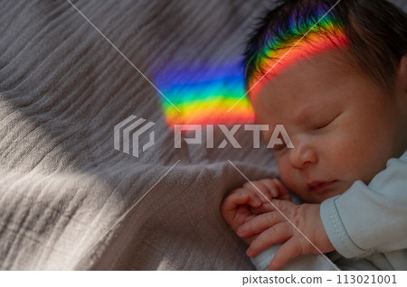 Close-up portrait of a newborn boy with a prism beam on his face. Rainbow. Close-up portrait of a newborn boy with a prism beam on his face. Rainbow. 113021001