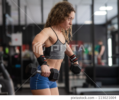 Muscular Caucasian forty year old woman doing exercises with dumbbells in the gym. Muscular Caucasian forty year old woman doing exercises with dumbbells in the gym. 113021004