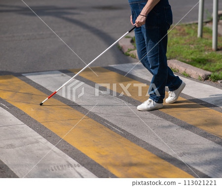 Close-up of the legs of a blind woman crossing the road at a crosswalk with a cane.  113021221