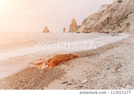 Large red jasper rock on the beach, with the sea in the background. Big Red Jasper Stone Close Up 113021277