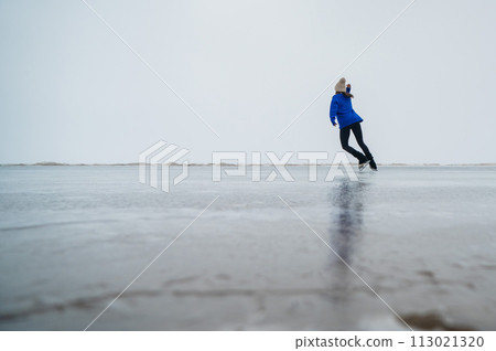 Caucasian woman in a blue sweater is skating on a frozen lake. The figure skater performs the program. 113021320