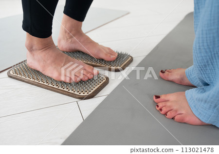 Caucasian woman stands on sadhu boards with therapist support. 113021478