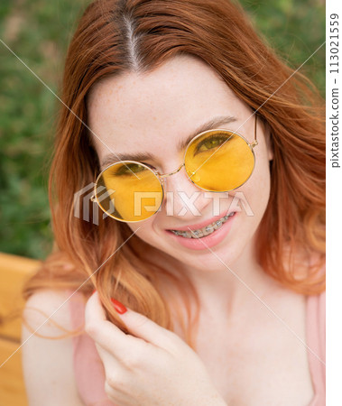 Beautiful young woman in yellow sunglasses smiling showing off braces on her teeth. Vertical photo. Beautiful young woman in yellow sunglasses smiling showing off braces on her teeth. Vertical photo. 113021559