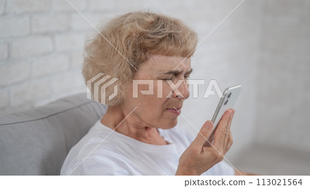 An elderly Caucasian woman suffers from myopia and tries to read a message on a smartphone. An elderly Caucasian woman suffers from myopia and tries to read a message on a smartphone. 113021564