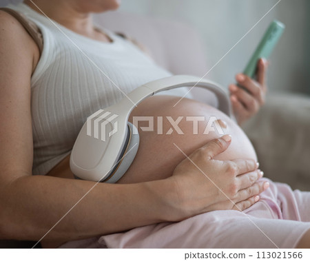 A pregnant woman turns on music for her child on a smartphone. Headphones on the tummy.  113021566