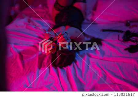 Couple in sexual BDSM games. Woman handcuffed in bed in red hanging neon light. Couple in sexual BDSM games. Woman handcuffed in bed in red hanging neon light. 113021617