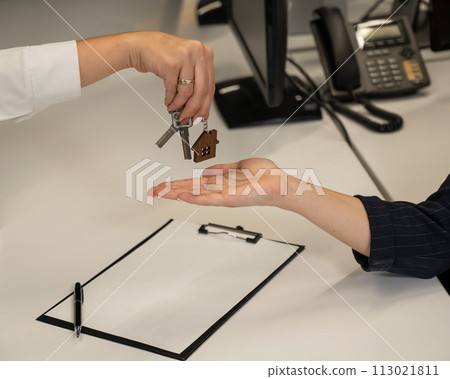 Real estate purchase transaction. The realtor hands the woman the keys to the house. Close-up of hands. 113021811