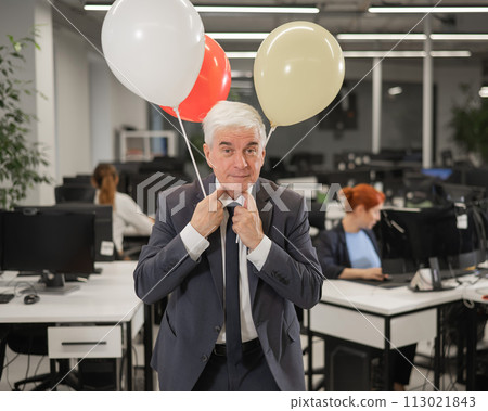 Portrait of a cheerful mature business man holding balloons in the office. Portrait of a cheerful mature business man holding balloons in the office. 113021843