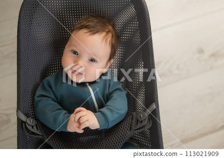 Cute newborn baby dressed in blue overalls sitting in a baby lounger. Cute newborn baby dressed in blue overalls sitting in a baby lounger. 113021909
