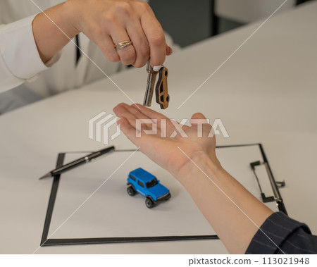 Car purchase deal. Salesman handing over keys to female customer.  113021948