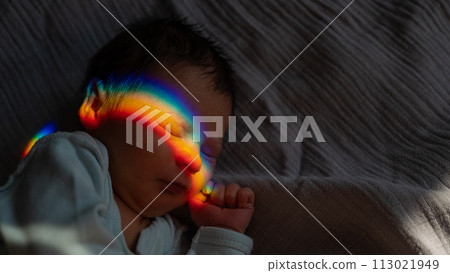 Close-up portrait of a newborn boy with a prism beam on his face. Rainbow. 113021949