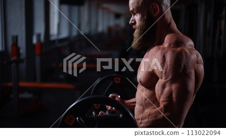 Caucasian bald topless man doing an exercise with a barbell in the gym. Bicep curls with weights. Caucasian bald topless man doing an exercise with a barbell in the gym. Bicep curls with weights. 113022094