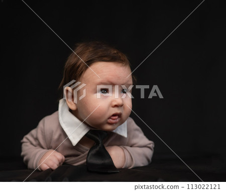 Portrait of a baby lying on his stomach wearing a tie on a black background. Portrait of a baby lying on his stomach wearing a tie on a black background. 113022121