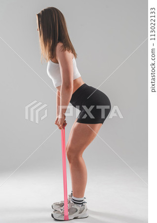 Caucasian woman doing exercises with fitness elastic band on white background. Vertical photo. 113022133