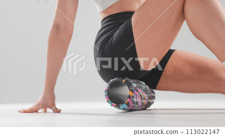 Faceless woman doing roller exercise for myofascial release on white background. Self-massage of thighs.  113022147