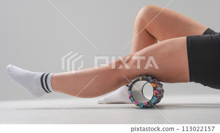 Faceless woman doing roller exercise for myofascial release on white background. Self-massage of legs.  113022157