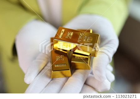 Gold bars in gloved hands close up. 113023271