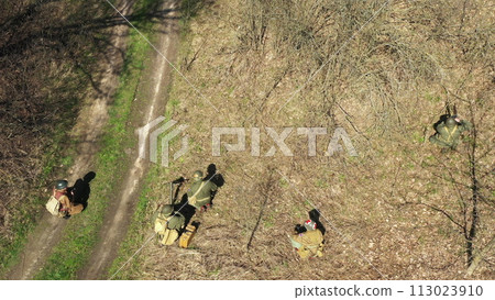 Men Dressed As US American Soldiers Of USA Infantry Of World War II sneaking around In spring Autumn Day. Soldiers prepare mortar for battle In dry grass. Aerial view elevated shot 113023910