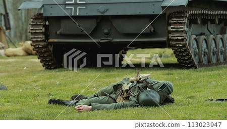 Close Up View On Re-enactor Dressed As German Wehrmacht Soldier Lies Slain In Reconstruction Of Battles World War Ii Near Wehrmacht Light Panzer Tank. German Infantry Soldier In World War Ii 113023947