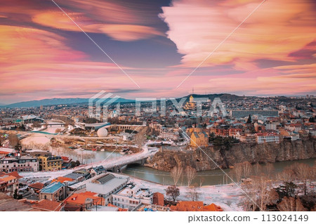 Tbilisi, Georgia. Amazing Cloud Trails In Sky. 6k Georgian Capital Skyline Cityscape. City During Sunset And Night Illuminations. Unusual Cloudy Effects Sky. Elevated Top View Of Famous Landmarks 113024149