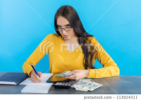 A rich young girl counts money at home at her desk for her next major financial investment. 113024311