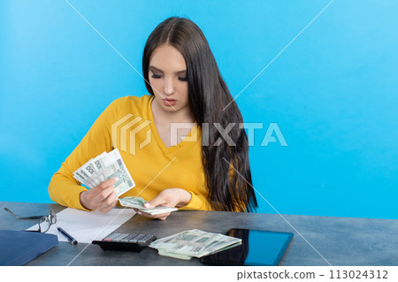 A rich young girl counts money at home at her desk for her next major financial investment. 113024312