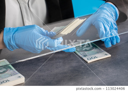 Hands of young cashier in protective gloves hand over bundles of banknotes. 113024406