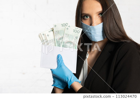 Businesswoman in a protective mask and protective gloves puts a bundle of paper banknotes into the envelope. Businesswoman in a protective mask and protective gloves puts a bundle of paper banknotes into the envelope. 113024470