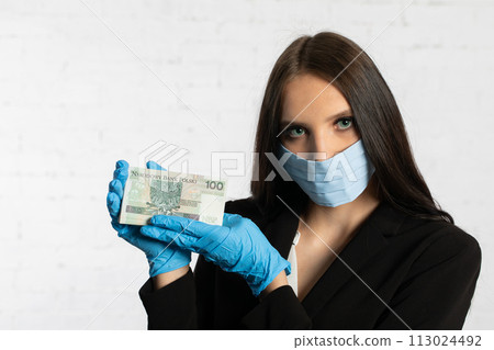 Businesswoman in a protective mask and protective gloves is holding a bundle of paper banknotes. 113024492