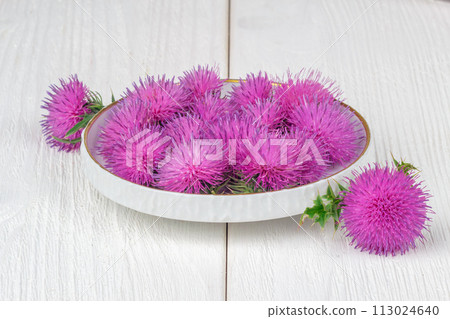 Silybum marianum (milk thistle) herb in a bowl.One of the most common uses of milk thistle is to treat liver problems.Alternative medicine concept on a white wooden table (selective focus). 113024640