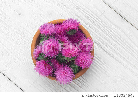 Silybum marianum (milk thistle) flowers in a wooden bowl.One of the most common uses of milk thistle is to treat liver problems.Alternative medicine concept on a white wooden table (selective focus). 113024643